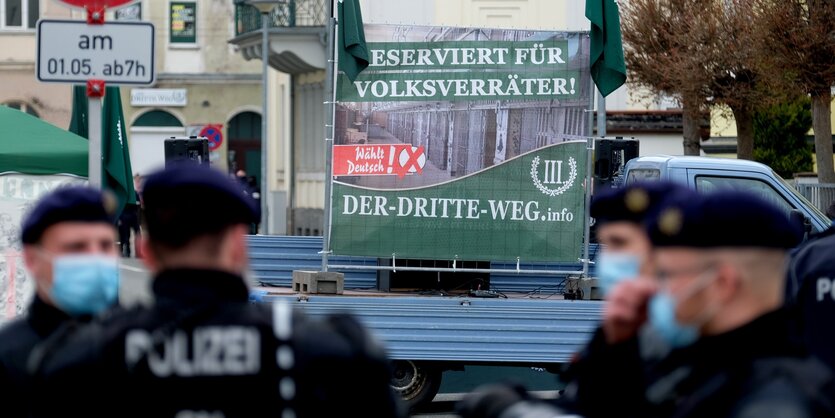 Drei Polizisten stehen vor einem Plakat der Partei der Dritte Weg, darauf die Aufschrift "Reserviert für Volksverräter"