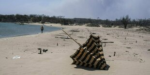 Ein einzelner Sonnenschirm liegt kopfüber am Strand, neben verbrannten Sonnenliegen und Sonnenschirmen