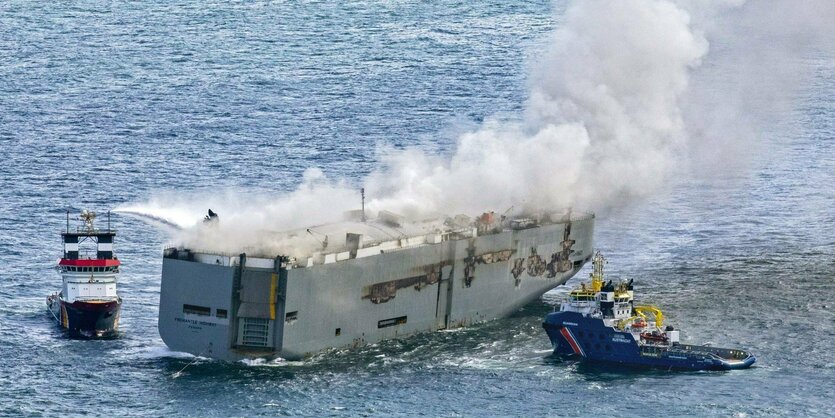 Ein brennendes Transportschiff mit Schleppern.