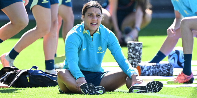 Sam Kerr in Trainingsjacke aud dem Rasen sitzend