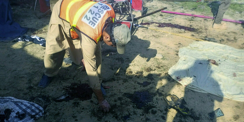 Ein Mann in Warnweste sucht gebückt etwas auf dem blutverschmierrten Boden am Ort der Bombenexplosion.