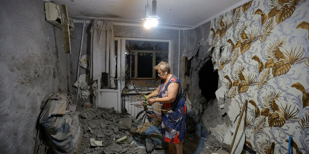 Eine Ukrainerin in ihrer Wohnung in Donetsk, in der Schutt liegt und ein großes Einschussloch der russischen Artielleri in der gemusterten Tapete klafft
