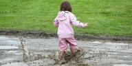 Kind in rosa Regenkleidung rennt durch eine Pfuetze