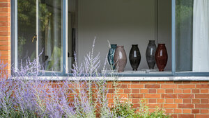 Blick von außen durchs Fenster ins Mies van der Rohe Haus, wo fünf bunte Vasen stehen