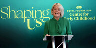 Alison Rose hält in einem grünen Kleid vor einem grünen Hintergrund eine Rede
