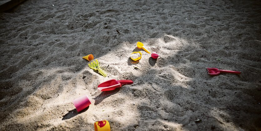 Buntes Sandspielzeug liegt in einer verlassenen Sandkiste