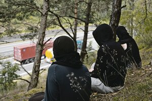 Menschen mit schwarzen Kapuzenpullovern sitzen auf einem Hang und blicken auf eine Autobahn.