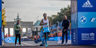 Marathonläufer Haftom Welday läuft durch einen Banner und über eine Zielline. Im Hintergrund sieht man das Brandenburger Tor.