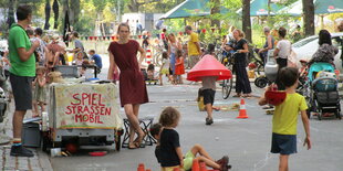 Kinder spielen auf der Straße. Auf einem kleinen Wagen steht "Spielstraßenmobil".