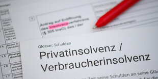 Ein Kugelschreiber liegt auf einem Antrag zur Eröffnung eines Insolvenzverfahrens und einem Informationstext über Privatinsolvenz / Verbraucherinsolvenz.