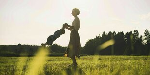 Eine glückliche Frau spielt mit ihrem Kleinkind auf einer Wiese