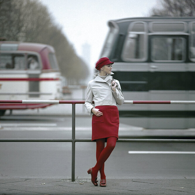 Modefoto von Arno Fischer: Eine Frau in Rot und Weiß gekleidet lehnt an einem Straßengeländer, im Hintergrund Verkehr