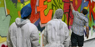 Zwei minderjährige Geflüchtete im Maleranzug stehen vor einer Graffiti-Wand