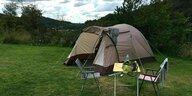 Ein Zelt steht auf einer Wiese mit Campingstühlen und einem Tisch davor