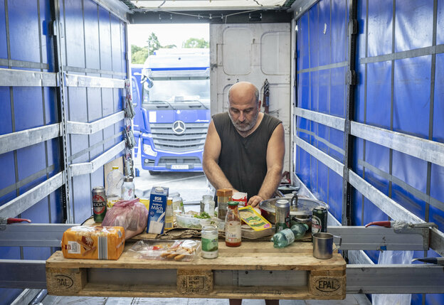 Ein Mann bereitet sich auf einer Ladefläche eines Lkw Essen zu