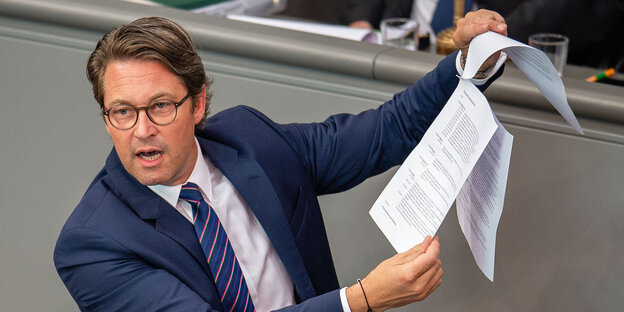 Andreas Scheuer spricht aufgeregt im Bundestag und hält dem Plenum einen Wust bedruckter Papiere entgegen