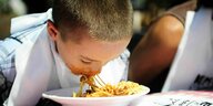ein Kind lehnt über einen Pastateller und isst die Pasta ohne Besteck