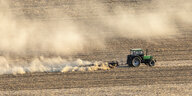 Landwirt grubbert nach der Ernte mit seinem Traktor den dürren Boden, Staubwolken aufwirbelnd