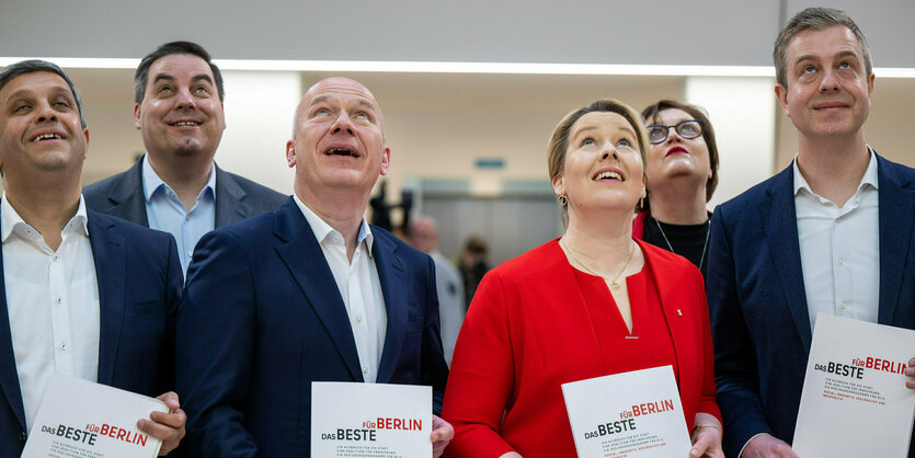 Menschen mit Anzügen und Schildern in der Hand schauen gespannt hoch