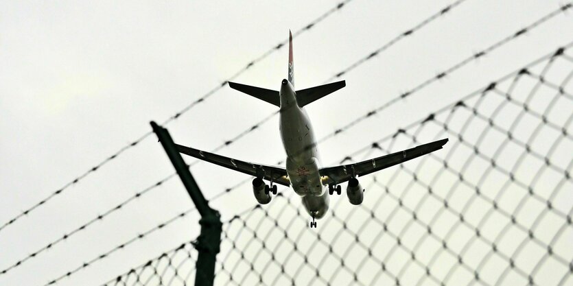 Ein Flugzeug fliegt über einen Stacheldrahtzaun - Symbolfoto