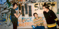 Drei junge Männer machen Faxen vor eine Graffitiwand