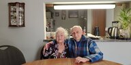 Efrem Steinbock und Frau Geta sitzen an einem großen Tisch in ihrer Wohnung, er hat den Arm um seine Frau gelegt