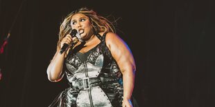 Lizzo steht auf der Bühne vor einem schwarzen Hintergrund und singt