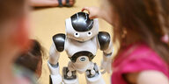 Ein Kind fasst den kleinen humanoiden Roboter "NAO" auf den Kopf