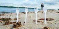 Einweg-Plastikgabeln stecken im Sand an einem Strand