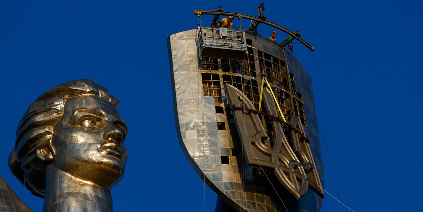 Bauarbeiter wechseln Wappen in der Skulptur Mutterland in Kyjiw