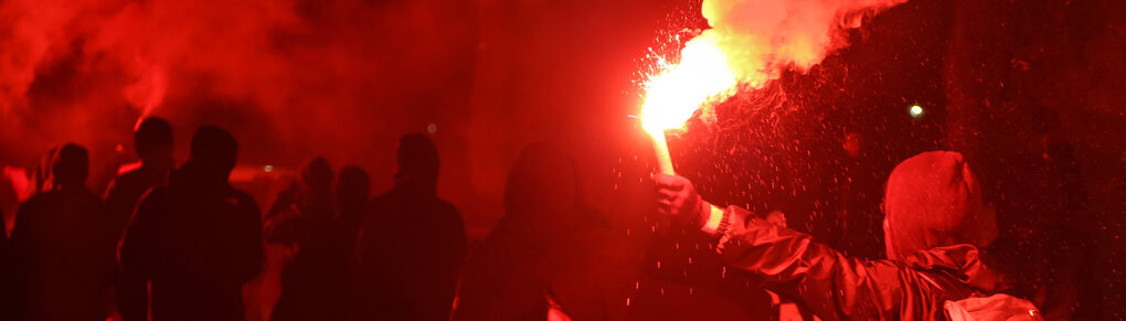 Ein:e Demonstrant:in mit einem Bengalo im Dunkeln