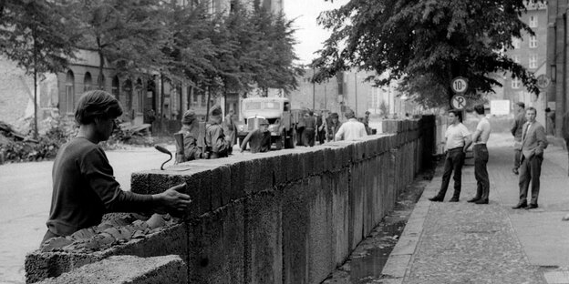 Unter den wachsamen Augen von bewaffneten Volkspolizisten sind 1961 Ostberliner Bauarbeiter dabei, eine Mauer entlang der Sektorengrenze auszubauen