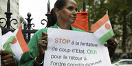 Eine Demonstrantin in Paris hält ein Plakat in den Händen, im Hintergrund Niger-Flaggen