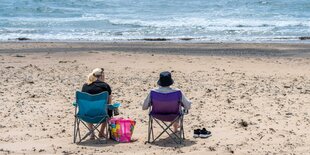 2 Personen sitzen am Strand