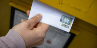 Eine Frau wirft einen Standardbrief in einen Briefkasten.