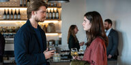 Ein junger Mann und eine junge Frau stehen sich gegenüber mit Weingläsern