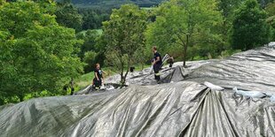 Einsatzkräfte breiten eine Folie über einen Hang aus