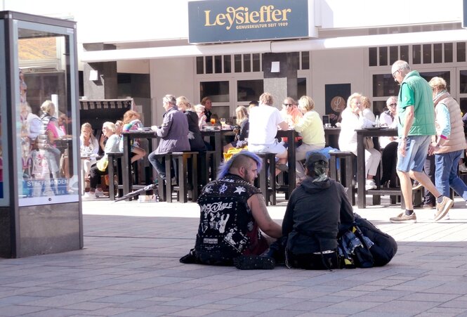 Rückenansicht von zwei Punks, die in der Fußgängerzone in Westerland sitzen und von den Passanten ignoriert werden