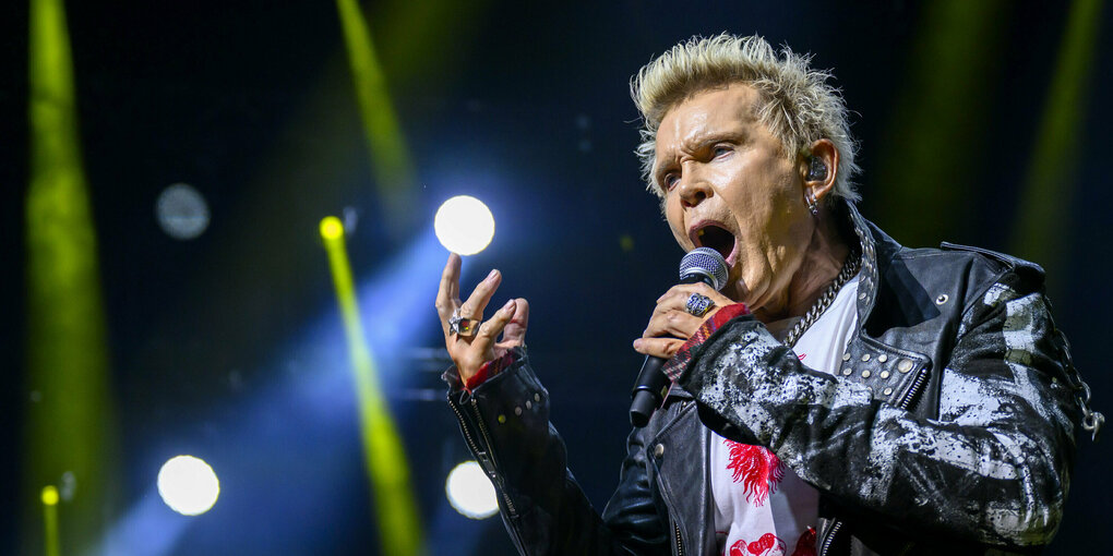 Billy Idol trägt immer noch blondierte Haare. Er steht mit seiner Band Generation Sex auf der Bühne, die auf dem Foto nicht zu sehen ist, und singt