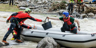 Ein Mann, der mit einem Boot über den Fluss transportiert wird, übergibt der Bergwacht die Handtasche einer Frau, während er aus dem Überschwemmungsgebiet evakuiert wird.