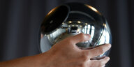 Eine Hand hält eine silberne Metalkugel, die die menschliche Iris scannen kann