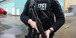 Polizist mit Waffe vor einem Gebäude.