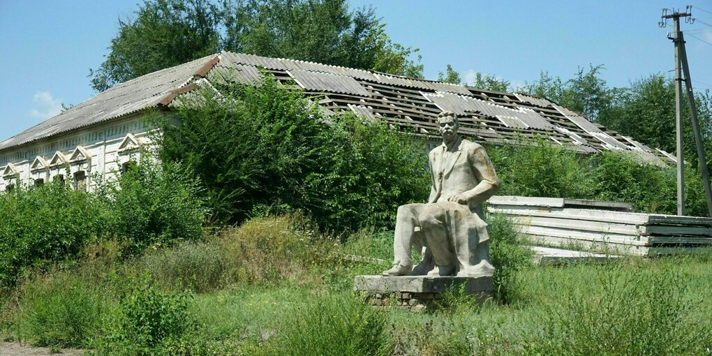 Die Figur von Maxim Gorki vor einem Gebäude, dessen Dach stark beschädigt ist