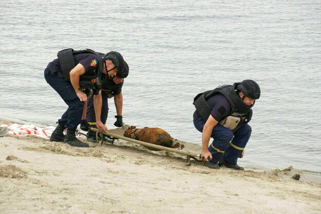 Zwei Männer am Strand mit einer Trage, auf der sie eine Mine transportieren