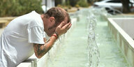Ein Mann kühlt sich an einem Springbrunnen ab.