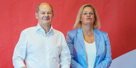 Olaf Scholz und Nancy Faeser stehen nebeneinander vor einem roten Hintergrund