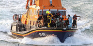 Ein Boot in auffälligem Orange fähre am 12. August im Ärmelkanal. Auf Deck sind mehrere Menschen, offenbar Retter und Gerettete
