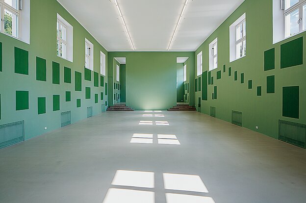 Blick in die Ausstellung von Bea Schlingelhoff im Münchener Kunstverein. Zu sehen sind leere, grüne Wände, auf denen die einstige Platzierung von Gemälden aus der Ausstellung "Entartete Kunst" in dunkler Farbe, wie Schatten, nachgezeichnet ist