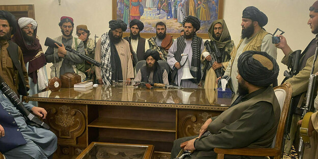 Bewaffnete Taliban sitzen nach der friedlichen Einnahme des Präsidenenpalastes in Kabul am 15. August 2021 um einen Schreibtisc,h