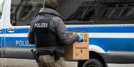 Polizist trägt Umzugskarton mit Akten zu einem Polizeiwagen